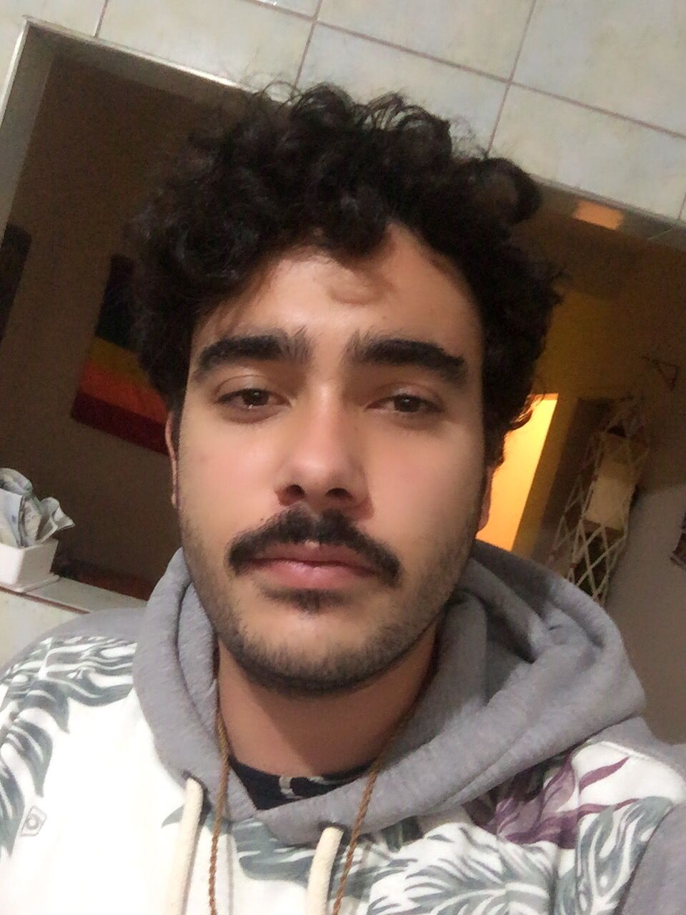 Homem, jovem, branco de cabelo cacheado e bigode.